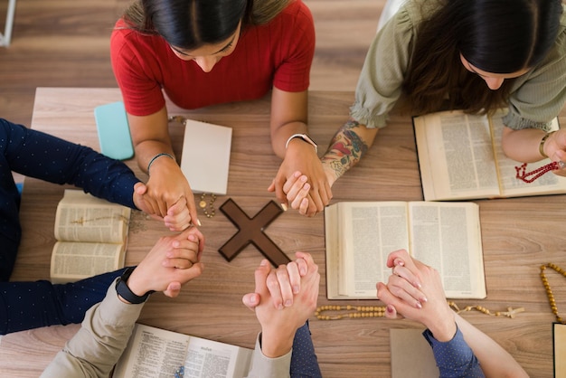 alto angulo hombres mujeres jovenes catolicos tomandose mano mientras rezan juntos alrededor mesa cruz cristiana 662251 1120